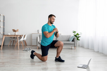 Happy millennial caucasian male doing leg exercises and watching video lesson in computer in living room