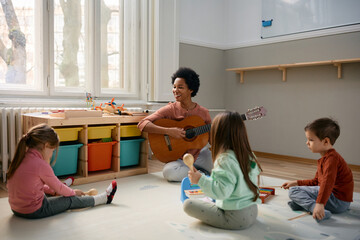 Happy black teacher and group of Caucasian kids enjoying during music class at kindergarten.