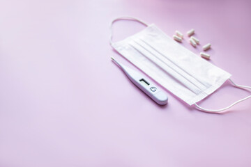 medical kit. medical mask, thermometer and pills on a pink background