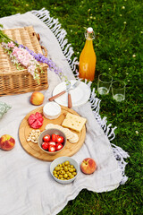 leisure and drinks concept - close up of food, drinks and basket on picnic blanket on grass