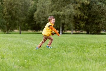 childhood, leisure and people concept - happy little boy running on green field at park