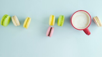 Top view of multicolored French Macarons cookies and a cup of coffee on a pastel blue background