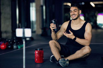 Fototapeta na wymiar Fitness And Nutrition Products. Arab Athlete Advertising Sport Shaker Bottle At Camera