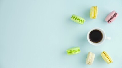Top view of multicolored French Macarons cookies and a cup of coffee on a pastel blue background