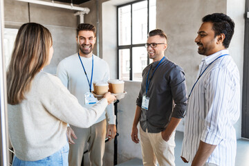 Obraz premium business, people and corporate concept - happy smiling colleagues with conference badges drinking takeaway coffee at office