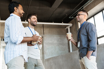 business, people and corporate concept - happy smiling businessmen or male colleagues with name tags drinking takeaway coffee at office