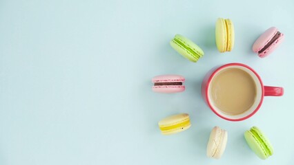 Top view of multicolored French Macarons cookies and a cup of coffee on a pastel blue background