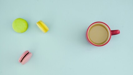 Top view of multicolored French Macarons cookies and a cup of coffee on a pastel blue background