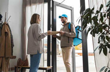 food shipping and people concept - happy delivery man with thermal insulated bag giving pizza box to female customer at home