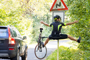 A falling cyclist bumps into a road sign next to road with traffic