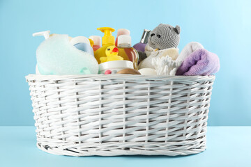 Wicker basket with baby cosmetic products and accessories on light blue background
