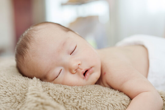 close-up photo of face of an Asian newborn sleeping happily on a brown carpet.