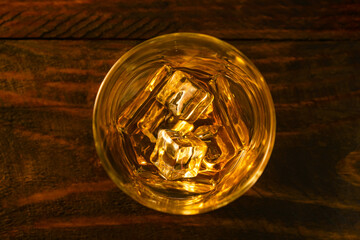 View from above a glass of whiskey and ice cubes on dark oak boards. Close-up.