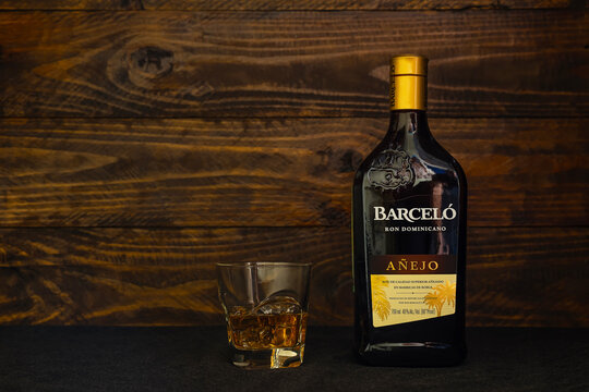 A bottle of Ron Barcelo, Anejo Dominican rum and a glass with ice on a dark wooden background. Ron Barcelo is a blend of rums aged in American bourbon oak barrels for varying amounts of time.