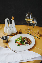 A dish is served on a table covered with a tablecloth in the restaurant. A plate with fish, scallops, appliances, sauces. There are glasses of wine and water nearby