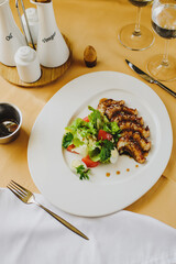 A dish is served on a table covered with a tablecloth in the restaurant. A plate with fish, scallops, appliances, sauces. There are two glasses nearby