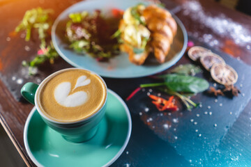 croissant sandwich breakfast with green salad and poached eggs, bacon and coffee