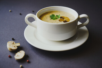 Mushroom cream soup in a white cup on a gray background. Next to mushrooms, peppers and a spoon