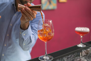 The bartender makes Aperol spritz summer cocktail in mister glass. Close up photo, process, bar. High quality photo