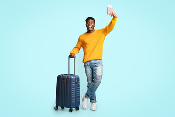 Cheerful african american guy with suitcase showing flight tickets