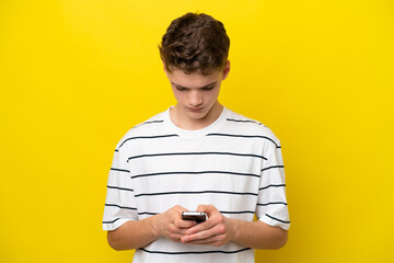 Teenager Russian man isolated on yellow background using mobile phone