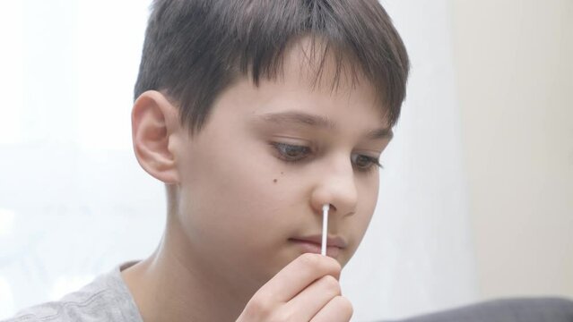 Teenage boy taking antigen self-test for Covid-19 with rapid diagnostic test kit. Kid using nasal swab while doing coronavirus PCR test at home before go to school lessons