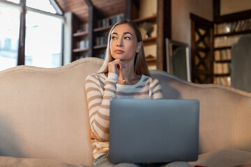 Pensive woman working on laptop at home