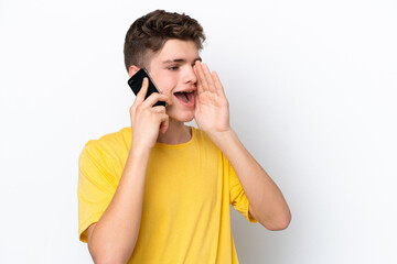 Teenager man using mobile phone isolated on white background shouting with mouth wide open to the side