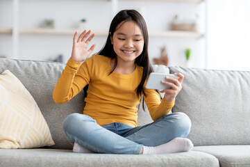 Obraz premium Positive asian kid having video conference with her friends