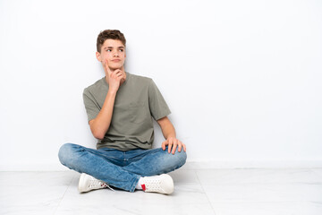 Teenager Russian man sitting on the floor isolated on white background thinking an idea while...