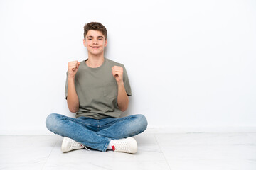 Fototapeta premium Teenager Russian man sitting on the floor isolated on white background celebrating a victory in winner position