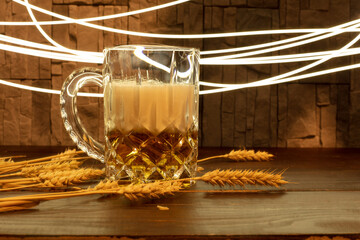 a glass of beer with foam on a wooden table against the background of wheat spikelets