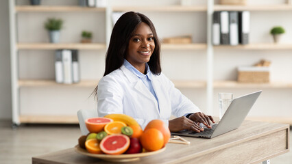 Healthy nutrition concept. African american weight loss consultant typing on laptop computer,...