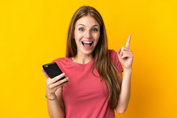 Young woman using mobile phone isolated on yellow background pointing up a great idea