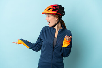 Young cyclist woman isolated on blue background with surprise expression while looking side - obrazy, fototapety, plakaty