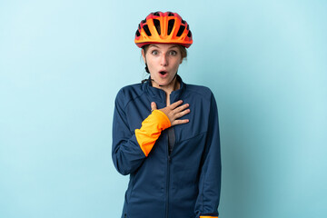 Young cyclist woman isolated on blue background surprised and shocked while looking right - obrazy, fototapety, plakaty
