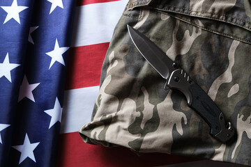 Folding tactical knife and military camouflage clothing on background American flag.