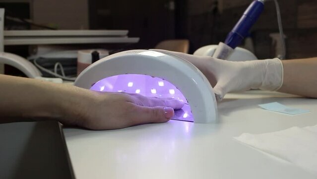 A client of a nail salon puts her hand with painted nails into a special ultraviolet lamp. Drying nail polish