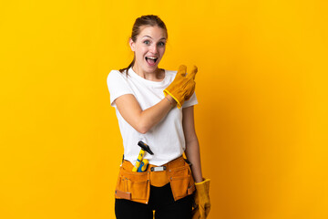 Young electrician woman isolated on yellow background surprised and pointing side