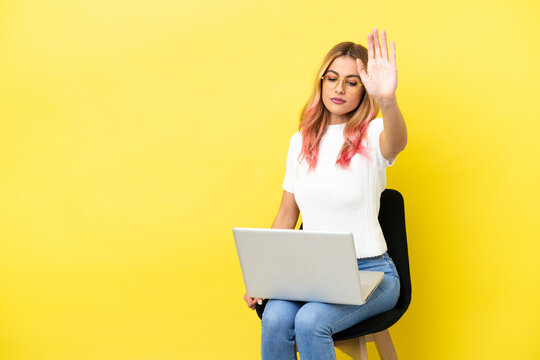 Young Woman Sitting On A Chair With Laptop Over Isolated Yellow Background Making Stop Gesture And Disappointed