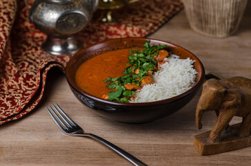 Tikka masala traditional butter chicken spicy meat food and rice with tomatoes in cast iron skillet on vintage wooden background.