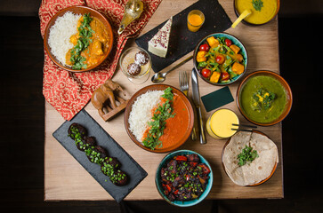 Assorted Indian home food, different dishes and snacks on wooden rustic table. Homemade Pilaf, butter chicken curry, palak paneer, chicken tikka, dal soup, naan bread, choice of chutney. Top view