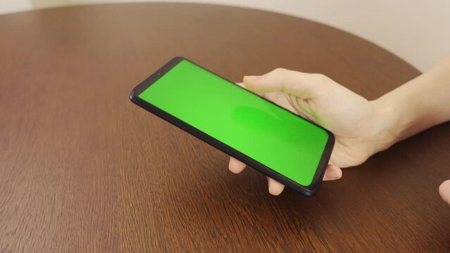 4k.Sides view. Woman using black smartphone with green screen.Hands of person scrolling up photos, pressing finger, reading social media internet, typing text or shopping online. Mobile phone in two