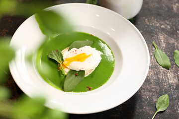 Green soup, creamy spinach soup with egg and goat cheese.
Appetizing dish on a plate, culinary photography. Food background.