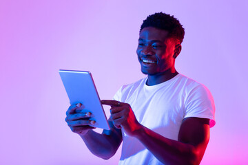 Portrait of joyful young black guy using tablet pc, studying or working remotely, having online...