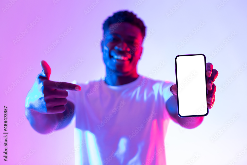 Poster handsome young black man pointing at smartphone with empty screen in neon light, selective focus. mo