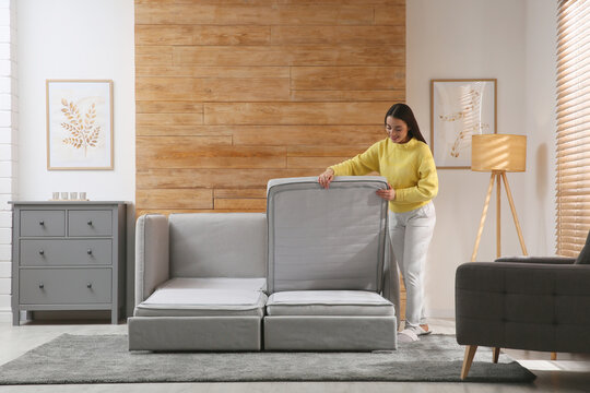 Young woman unfolding sofa into a bed in room. Modern interior