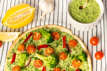vegan pizza with broccoli and spinach pesto sauce, tomatoes on a white table