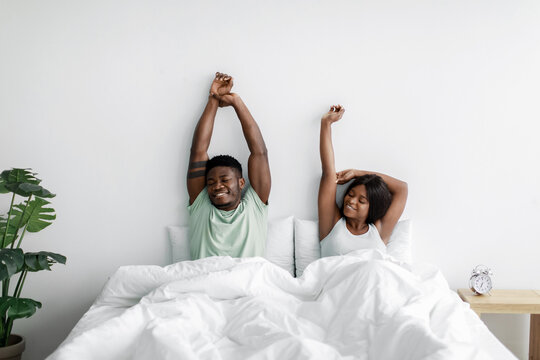 Cheerful millennial african american wife and husband woke up after sleep, stretching bodies on bed