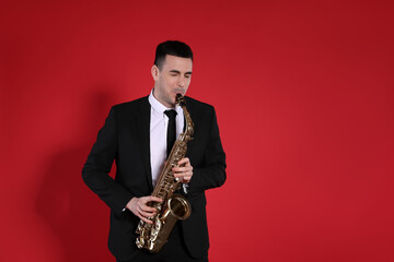 Fototapeta na wymiar Young man in elegant suit playing saxophone on red background